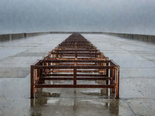 A rusting crush barrier on an empty concrete terrace in the rain