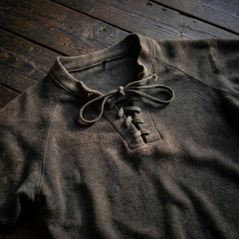 A thick antique wool football jersey with a laced collar laid on dark wooden boards